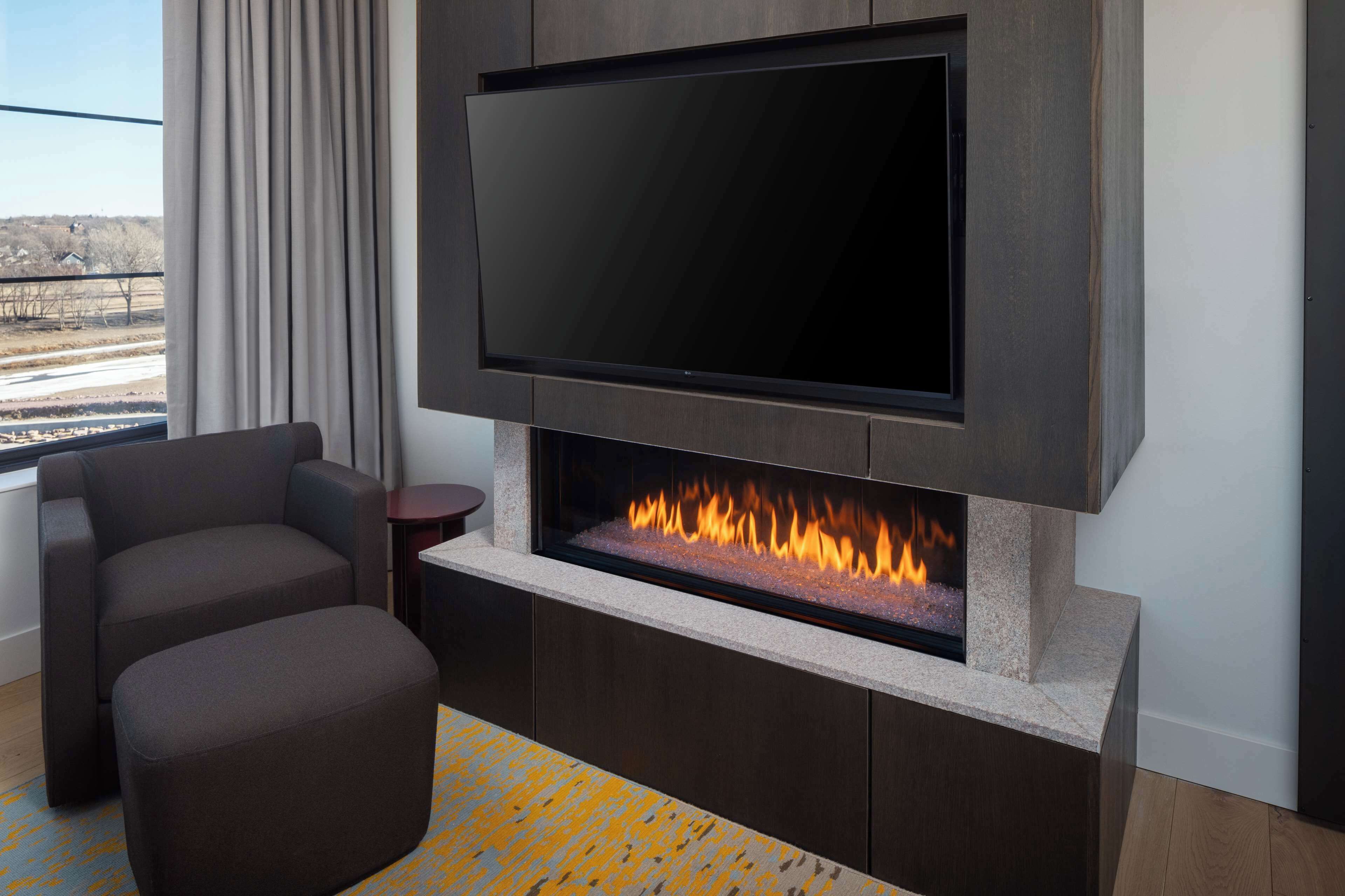A modern living room with a flat-screen TV mounted above a fireplace, comfortable seating, and a view of the outdoors.