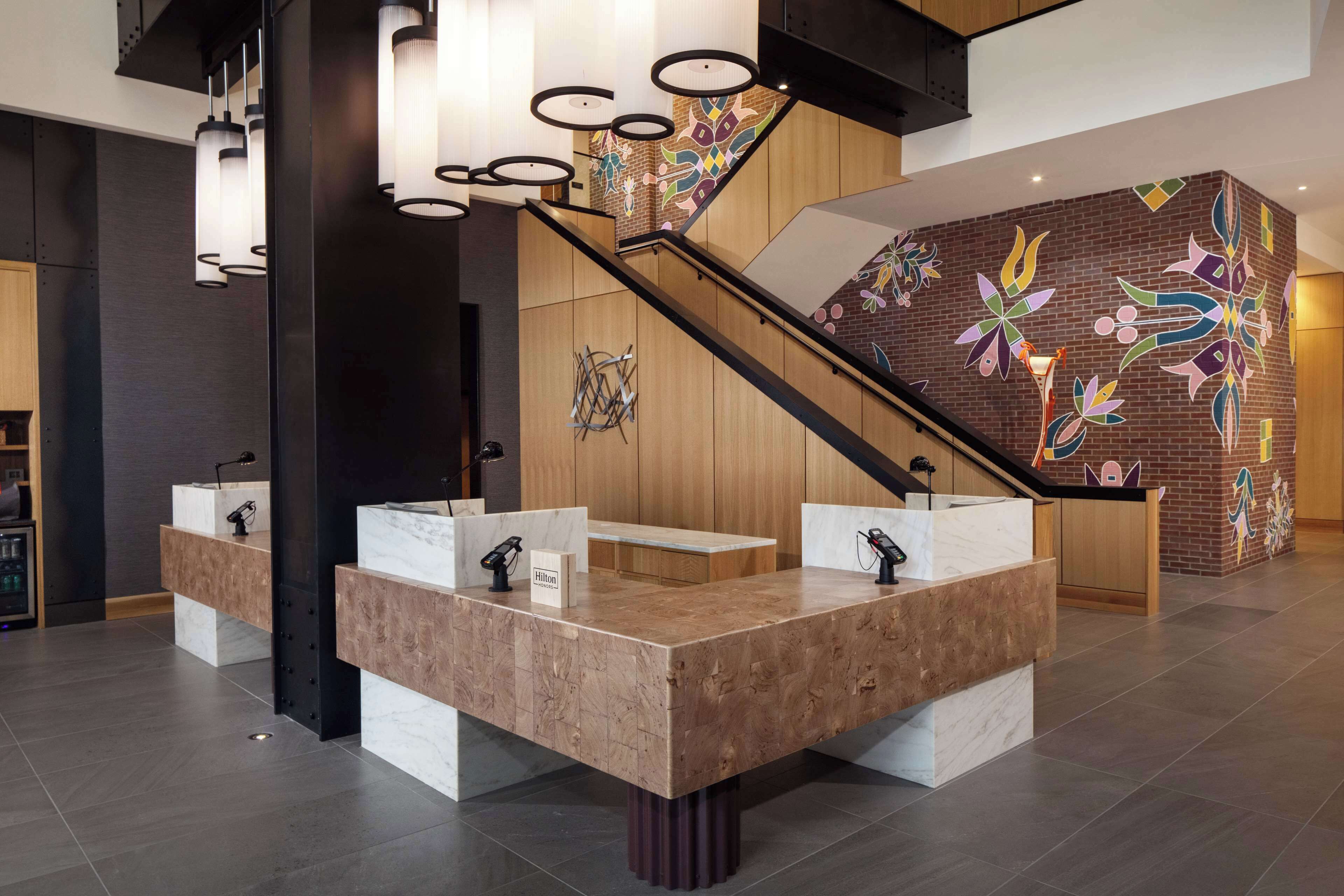 Un moderno vestíbulo de hotel con un mostrador de recepción central, una escalera y un mural de colores.