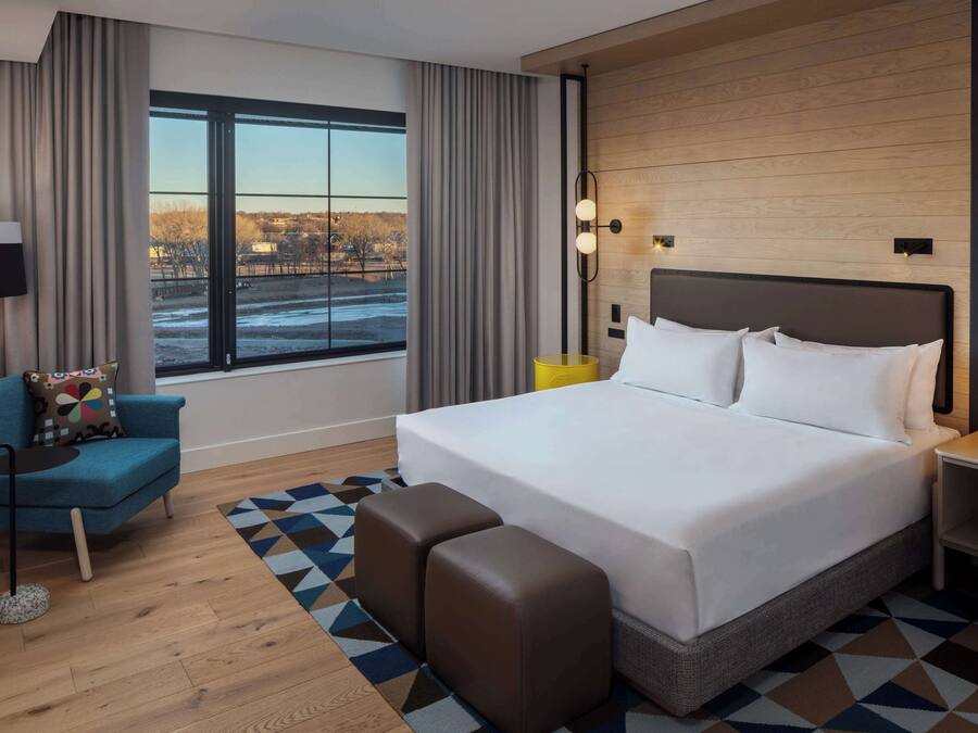 Un hotel moderno con una cama grande, un sillón azul, una mesita y vistas a un paisaje nevado a través de la ventana.