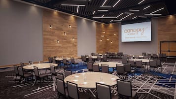 Une salle de conférence dotée de plusieurs tables et chaises, d’un grand écran affichant le nom de l’hôtel et d’un design moderne au niveau du plafond.