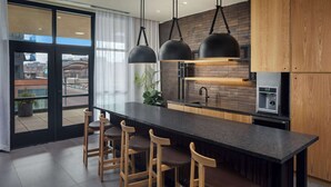 A modern kitchen with a central island, bar stools, pendant lights, and a view through large glass doors. - Canopy By Hilton Sioux Falls Downtown (Sioux Falls)