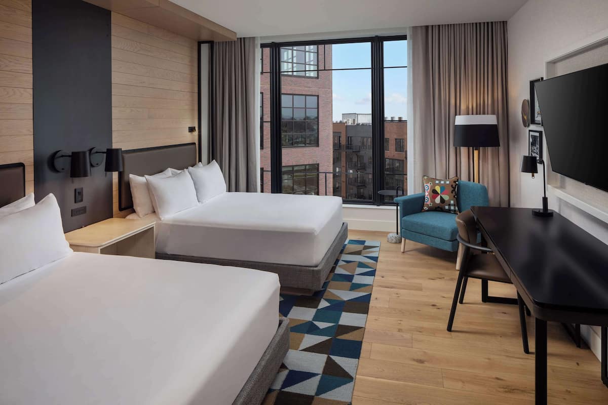 Een hotelkamer met twee bedden, een bureau, een televisie en uitzicht op de stad.