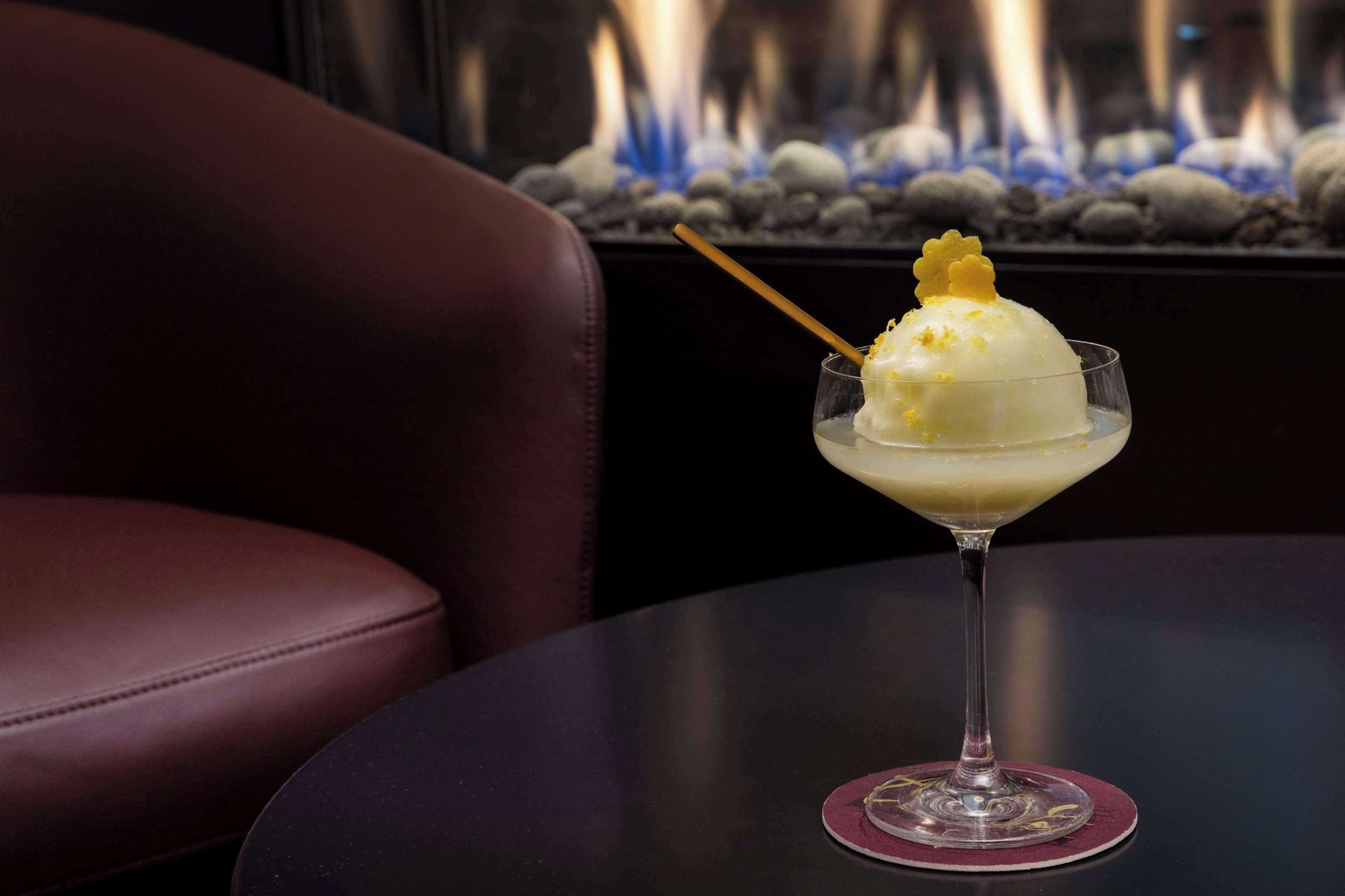 A dessert in a glass on a table with a chair in the foreground and a fire feature in the background.