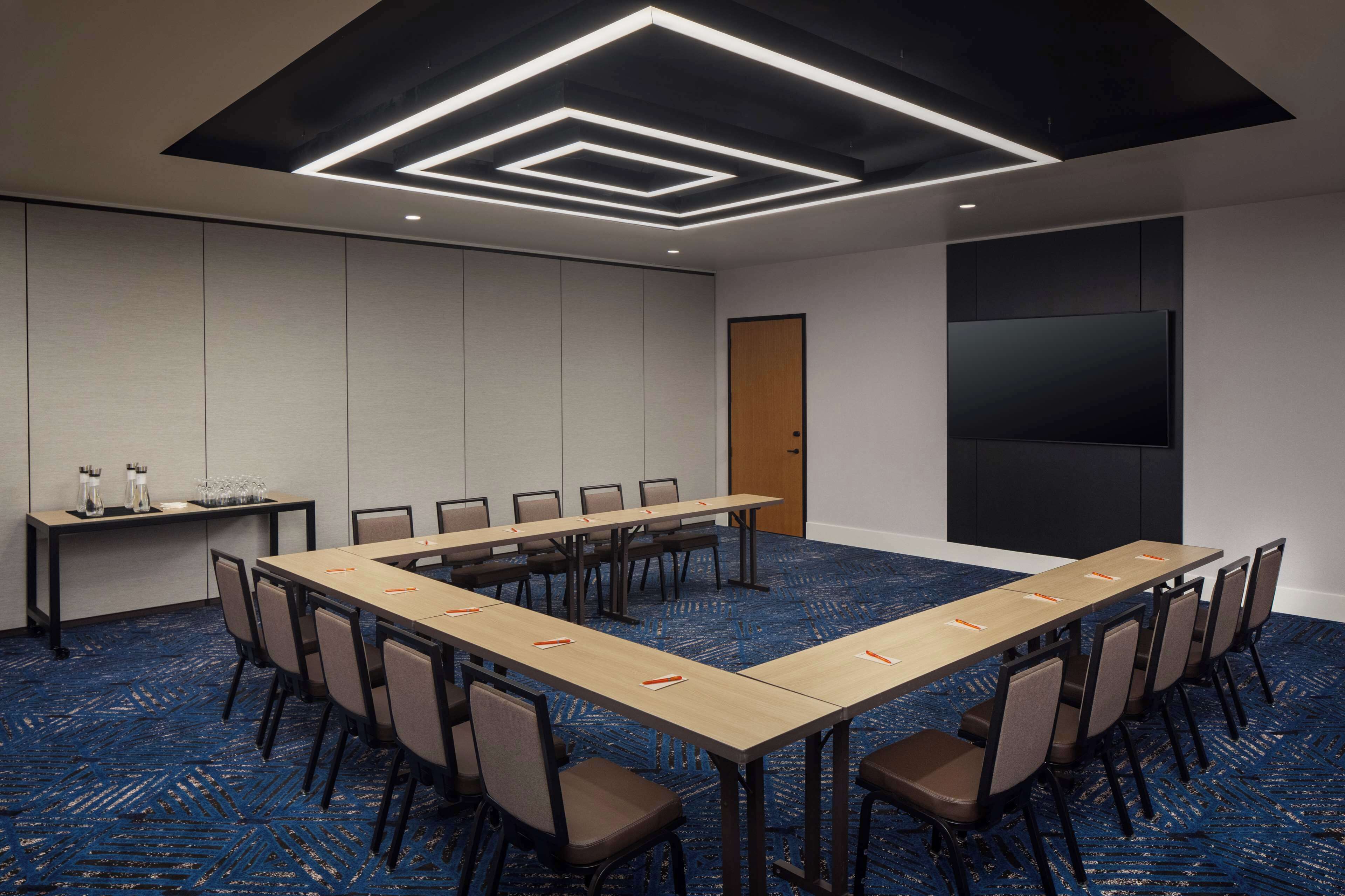 A conference room with a long table, chairs, a projector screen, and a carpeted floor.