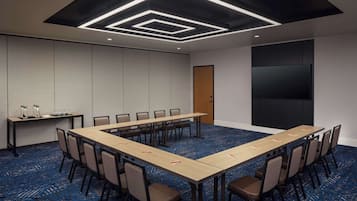 A conference room with a long table, chairs, a projector screen, and a carpeted floor.