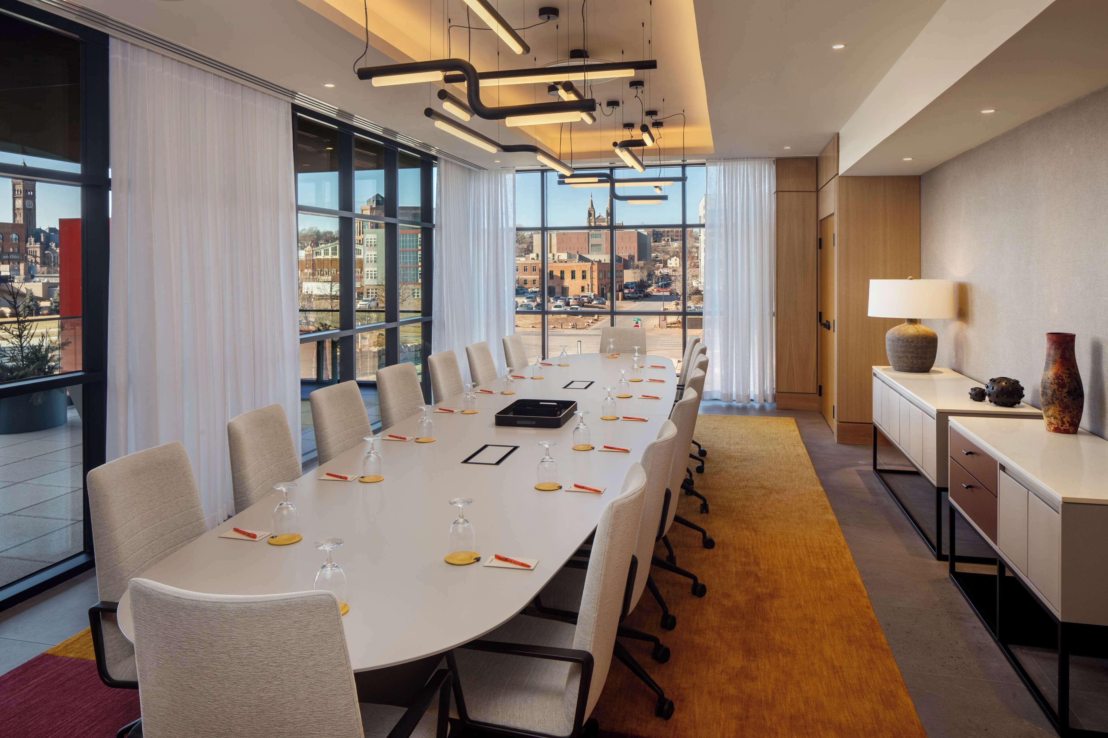 A conference room with a long table, chairs, a lamp, and a view of the city through large windows.