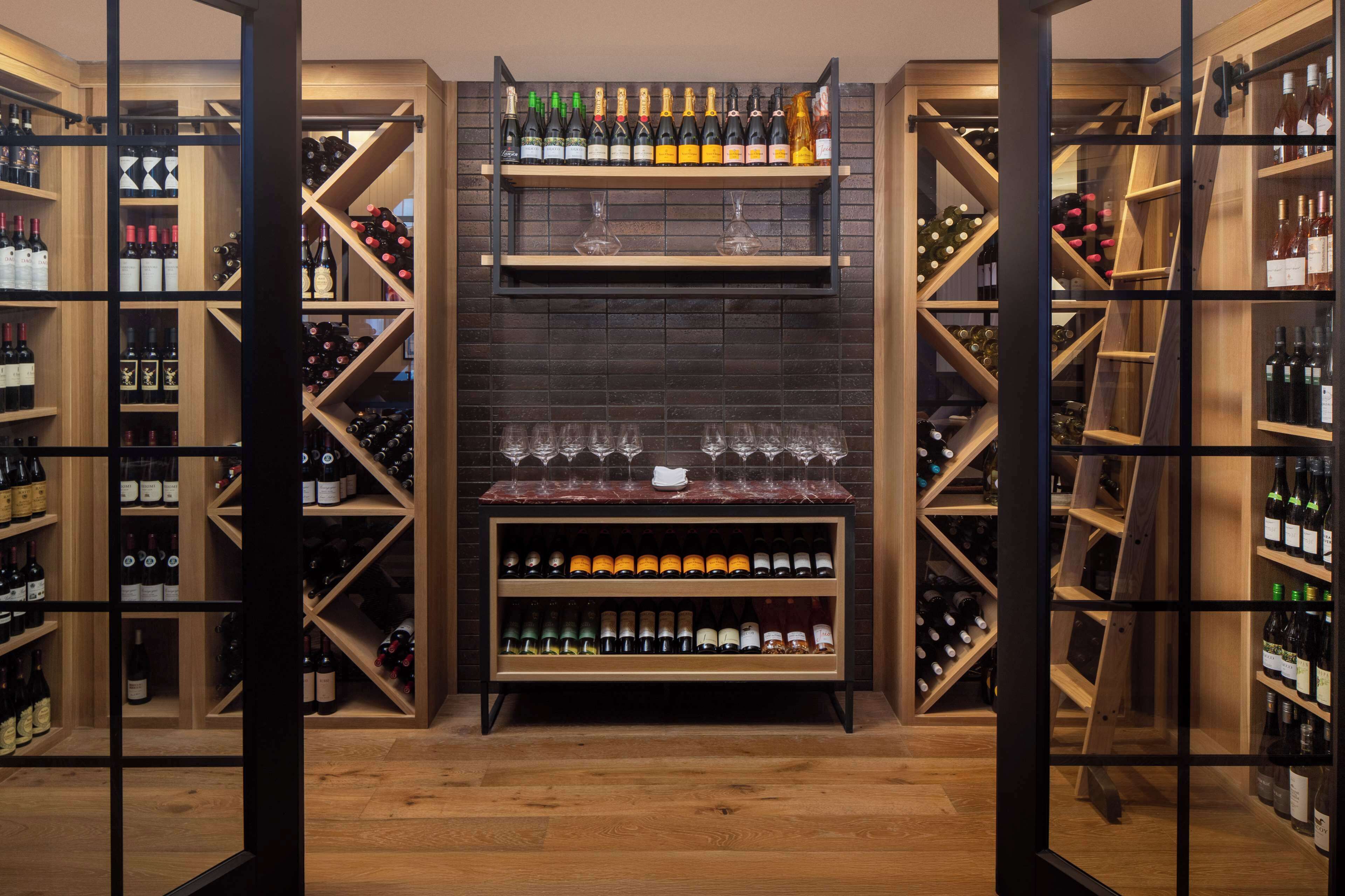 A wine cellar with wooden shelves and racks, displaying various bottles and glasses.