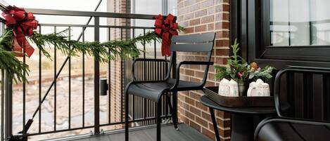 Un balcón con una silla, una mesa con tazas y un adorno navideño con lazos rojos.