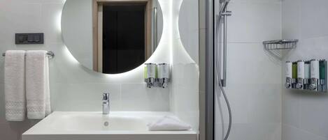 A modern bathroom with a white sink, a round mirror, a handheld showerhead, and a towel rack.