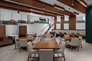 A modern indoor dining area with wooden tables and white chairs, a staircase, and green plants on the walls.
