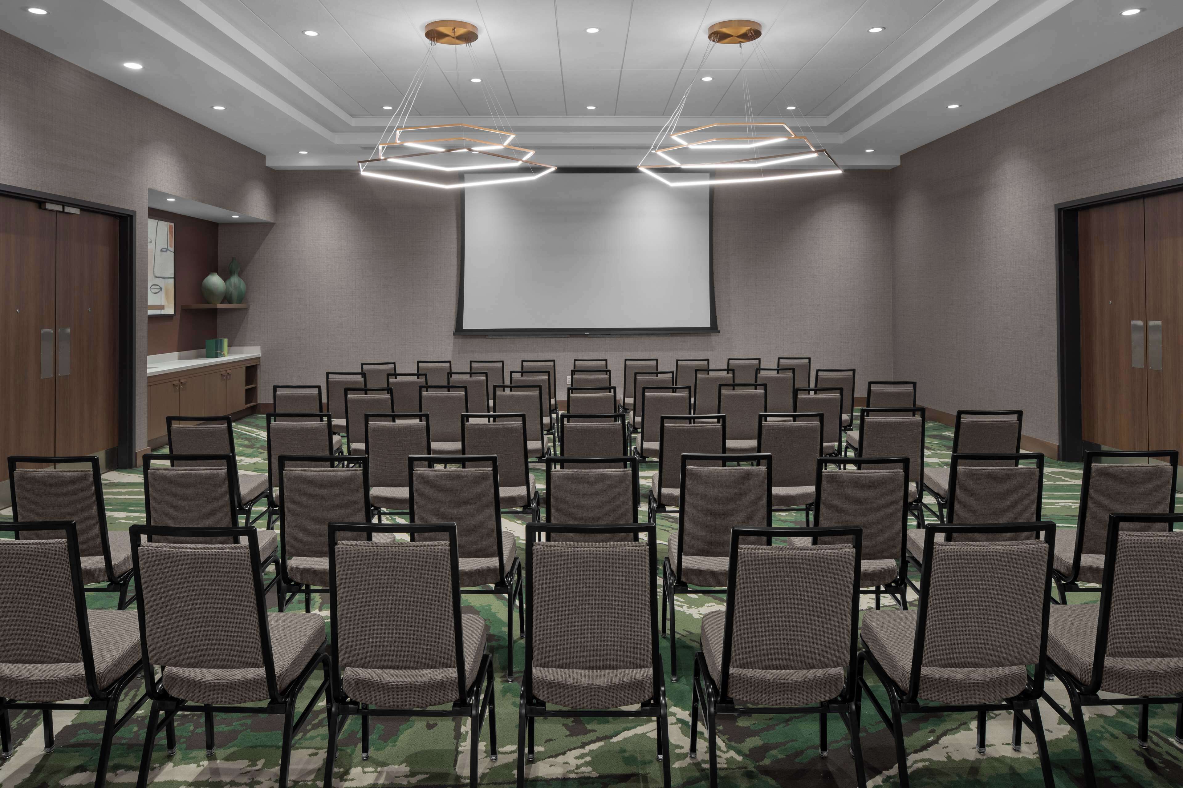 A conference room with rows of chairs, a large screen, and modern lighting fixtures.
