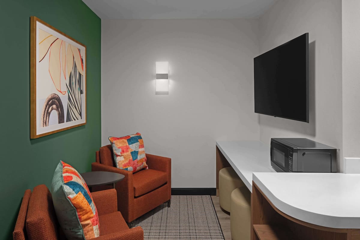 A compact room with a sofa, a small table, a microwave, and a flat-screen TV mounted on the wall.