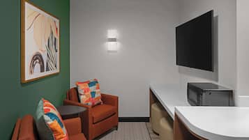 A compact room with a sofa, a small table, a microwave, and a flat-screen TV mounted on the wall.