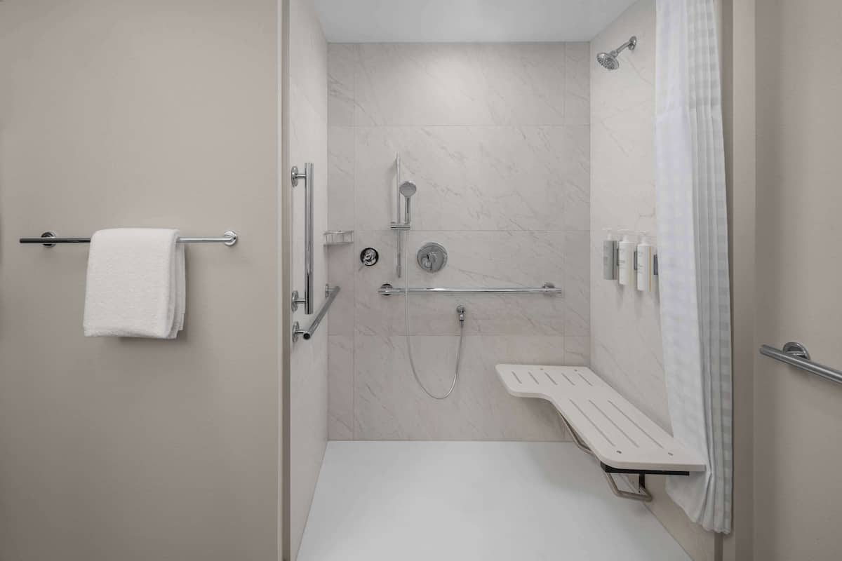 A modern bathroom with a shower, a bench, and a towel rack.