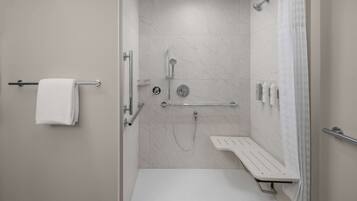 A modern bathroom with a shower, a bench, and a towel rack.