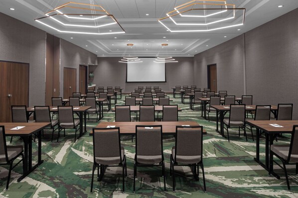 A conference room with multiple tables and chairs, a large screen, and modern lighting fixtures. - Embassy Suites By Hilton Madison Downtown (Madison)
