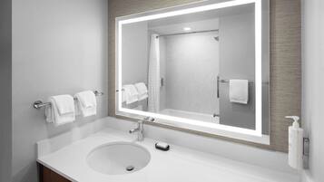 A modern bathroom with a large mirror, white sink, and two towels hanging on a towel bar.