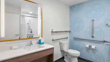 A modern bathroom with a white sink, mirror, and toilet. It includes a handrail and a towel rack.