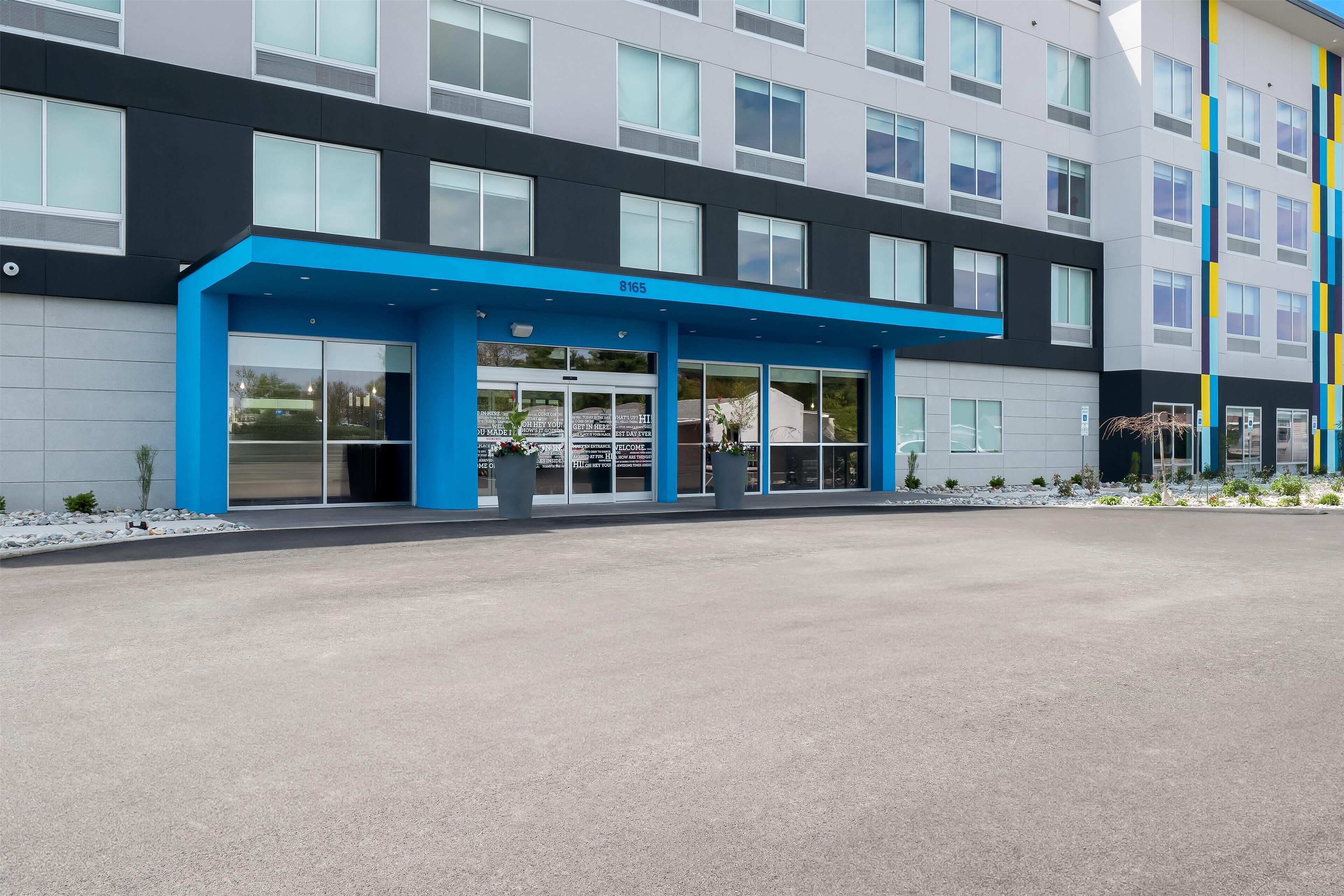 A modern building with a blue entrance canopy, large windows, and a flat roof.