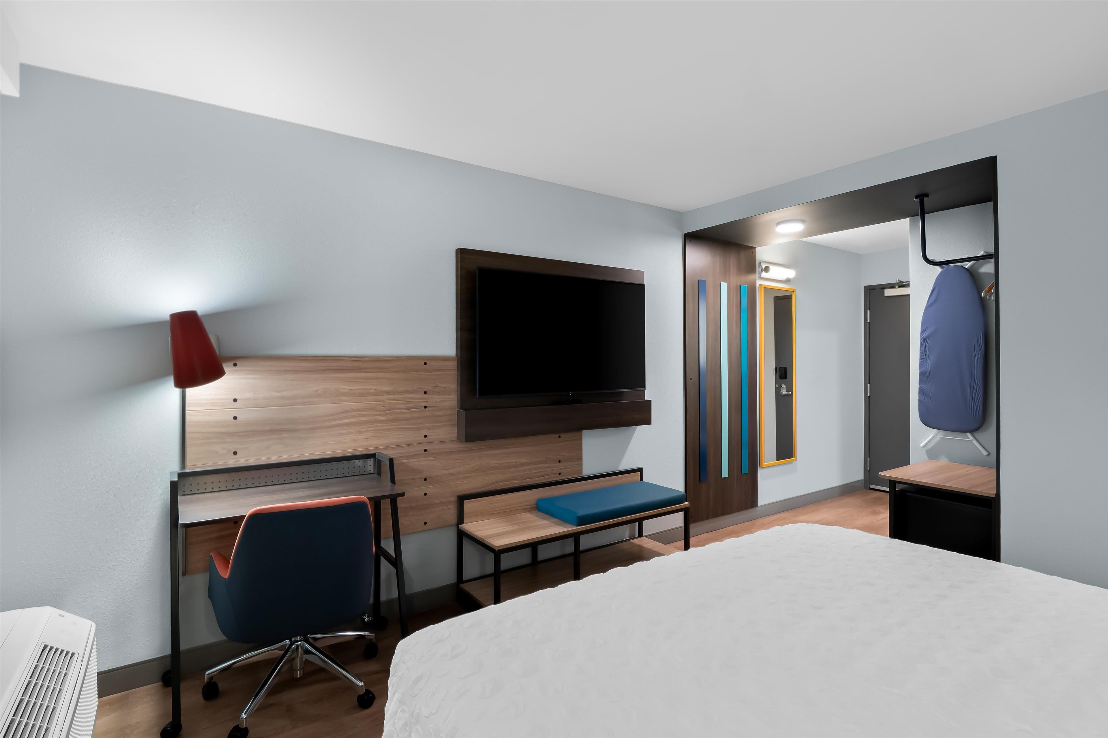 A modern hotel room with a bed, desk, chair, TV, and a mirror.