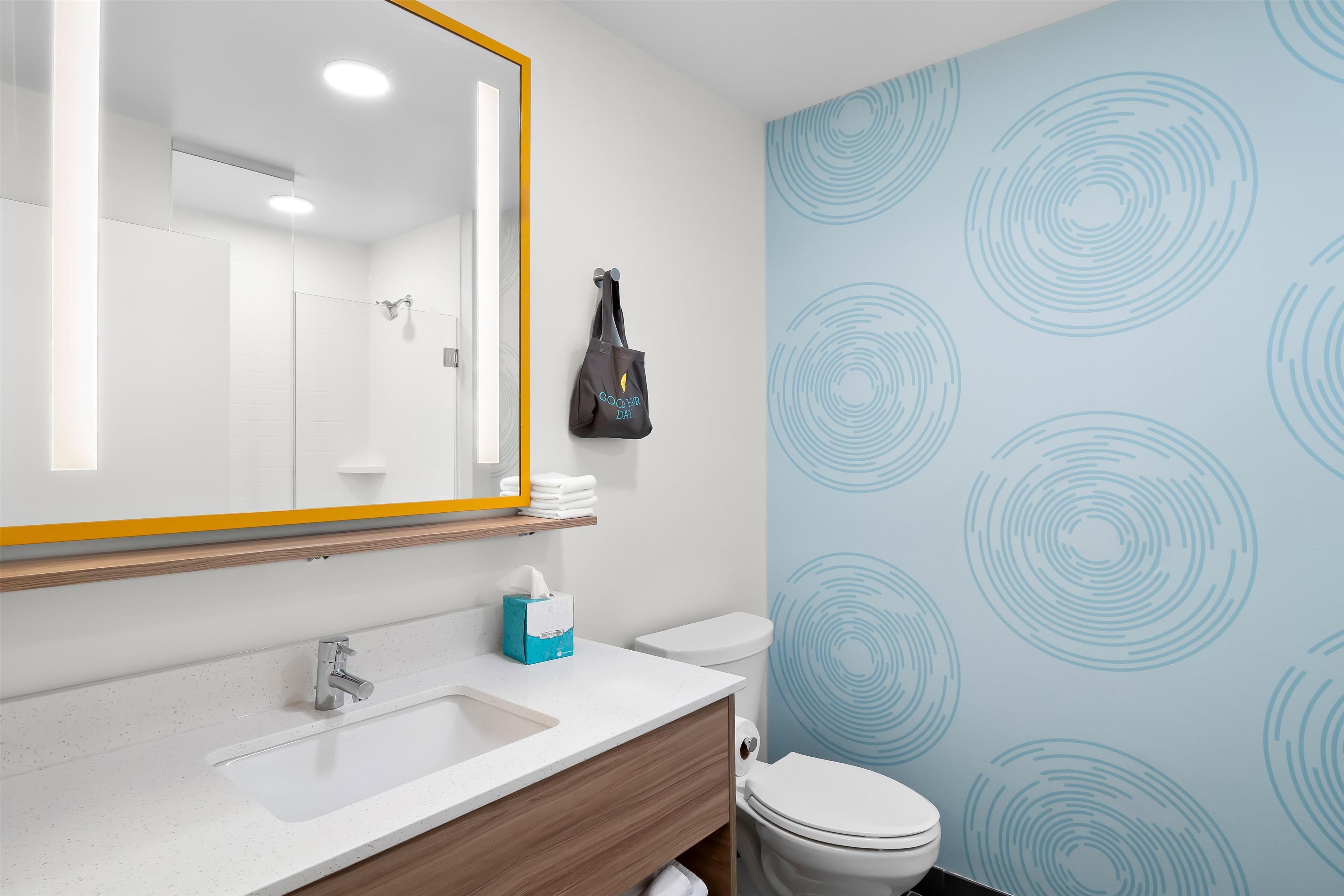 A bathroom with a white sink, mirror, and toilet. There is a towel rack with a bag on it.