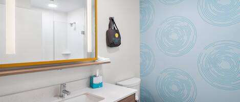 Un baño con lavamanos blanco, tocador de madera, espejo con marco amarillo, inodoro y pared con diseño circular.