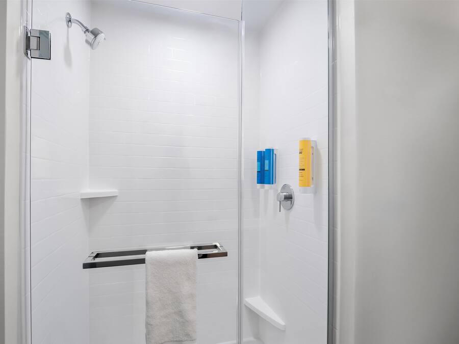 Une salle de bain moderne avec des murs recouverts de carreaux blancs, une douche en verre, un porte-serviettes et une étagère contenant des articles de toilette.