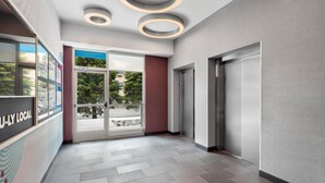 A modern lobby with a glass door entrance, a reception desk, and a wall-mounted elevator. - Tru By Hilton Wauseon (Wauseon)