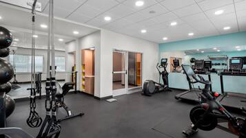 A gym with various exercise equipment, including treadmills and stationary bikes, and a weightlifting area with barbells and weights.