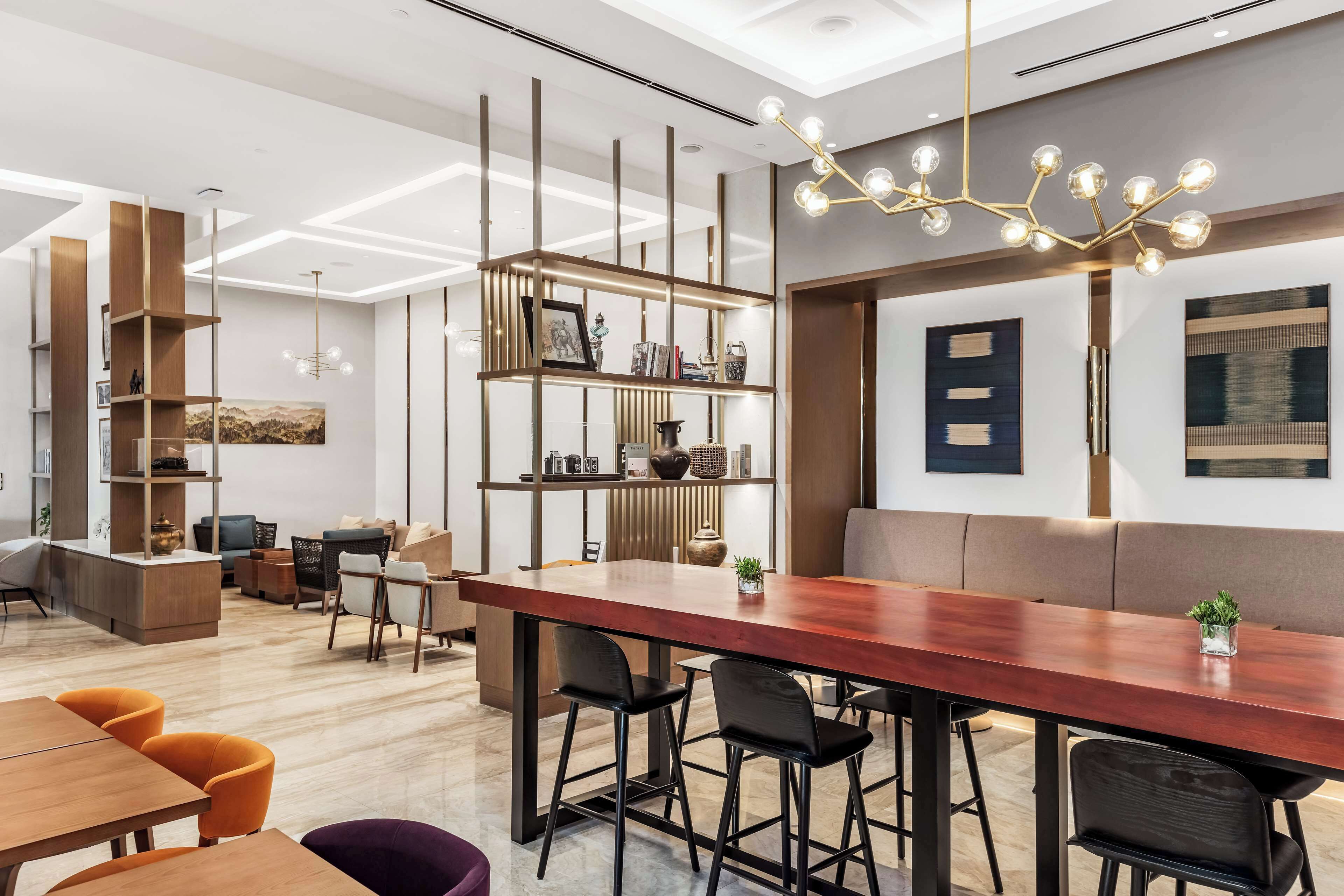 A modern interior with a long wooden bar, black bar stools, and a seating area with a sofa and chairs.
