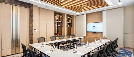 A conference room with a long table, chairs, a projector screen, and built-in shelving.
