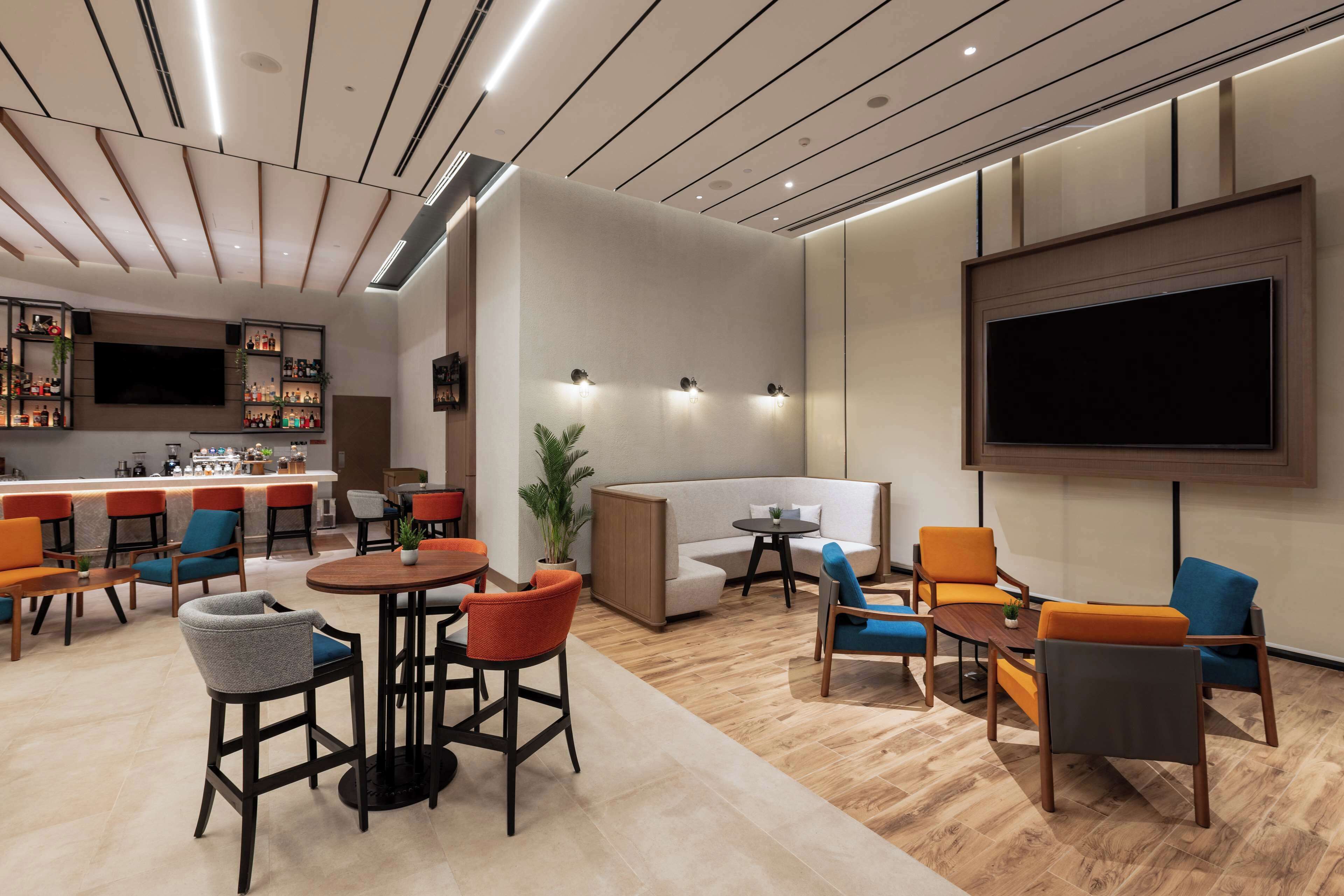 A modern lounge area with a bar, seating arrangements, and a large TV screen.