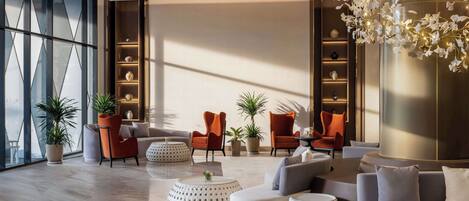 A modern lounge area with a sofa set, two orange armchairs, and a coffee table. There are potted plants and a decorative light fixture.
