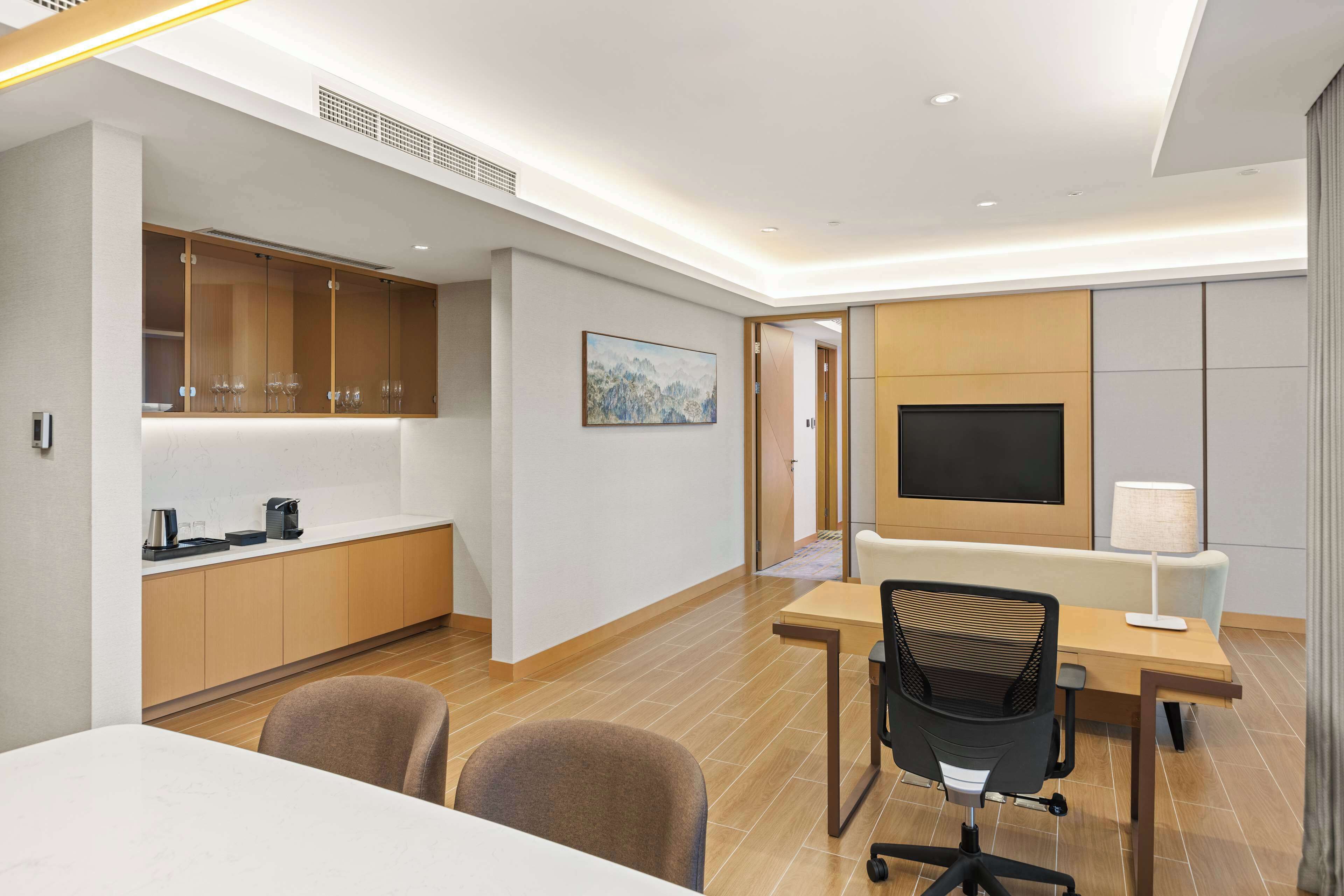 Una habitación de hotel moderna con zona de comedor, televisor y escritorio.