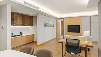 A modern hotel room with a dining area, a TV, and a desk.