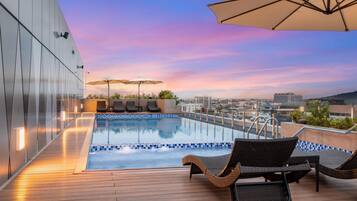 Relax by the rooftop pool with a stunning city view, surrounded by lounge chairs and umbrellas.
