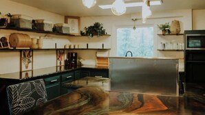 A modern kitchen with a marble countertop, hanging light fixtures, and shelves with decorative items. - Enchanting Forest Retreat (Anchorage)