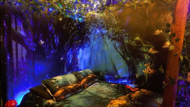 A cozy room with a bed, a small table with a mushroom decoration, and a wall with a forest-themed mural. - Enchanting Forest Retreat (Anchorage)