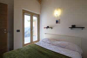 A bedroom with a bed, a window, a door, and a wall-mounted shelf. - Artemisia in Parzanica (Parzanica)