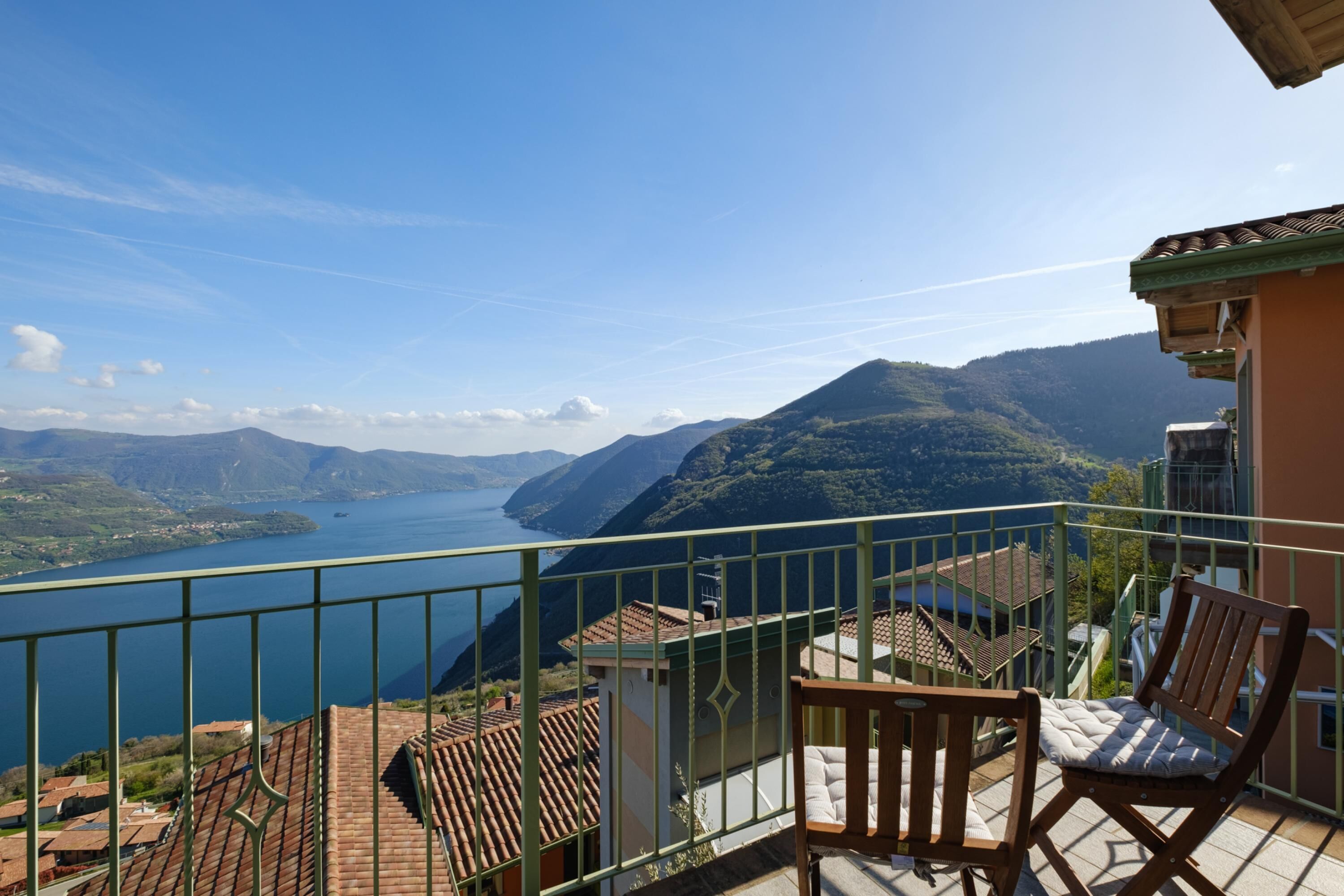 Un balcon avec vue sur un lac et des montagnes, des chaises en bois et un toit recouvert de tuiles.