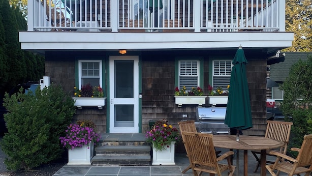 Une maison à deux étages avec un balcon, une terrasse dotée d’une table et de chaises, et un barbecue.