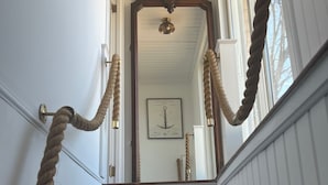 Un escalier doté d’une main courante en corde, de murs blancs et d’un luminaire au plafond.