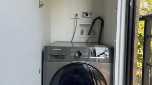 Una lavadora Samsung compacta en un lavadero pequeño con ventana y puerta.