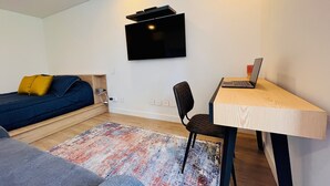 Una habitación moderna y funcional con cama, escritorio con computadora portátil y televisor montado en la pared.