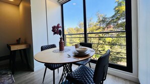 Un comedor con una mesa redonda, sillas acolchadas negras, un florero con flores y vistas a árboles a través de amplios ventanales.