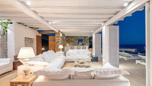 En hyggelig og godt oplyst lounge med hvide møbler, en stenvæg og havudsigt.