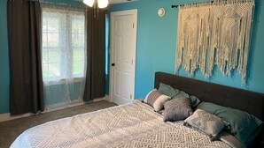 Un dormitorio con cama, cortinas, ventilador de techo y un tapiz de macramé en la pared.