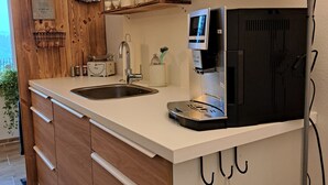 A modern kitchen with wooden cabinets, a built-in sink, a coffee machine, and a TV mounted on the wall. - Ferienwohnung im Allgäu mit Direktem Blick auf den Hochgrat in Ruhiger Lage! (Argenbühl)