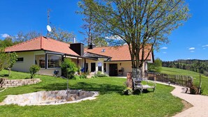 A two-story house with a red-tiled roof, a stone fountain, and a wooden fence. - Ferienwohnung im Allgäu mit Direktem Blick auf den Hochgrat in Ruhiger Lage! (Argenbühl)