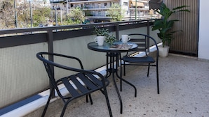 A balcony with two black metal chairs and a small round table, a potted plant, and a white wall with a window. - Boutique Stylish 1 Bd Apt in Patisia (Athens)